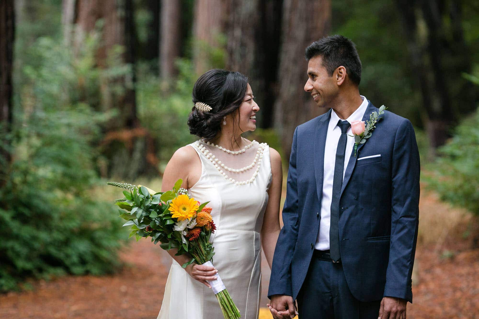 Bride with bouquet and groom in blue suit looking at each other and smiling