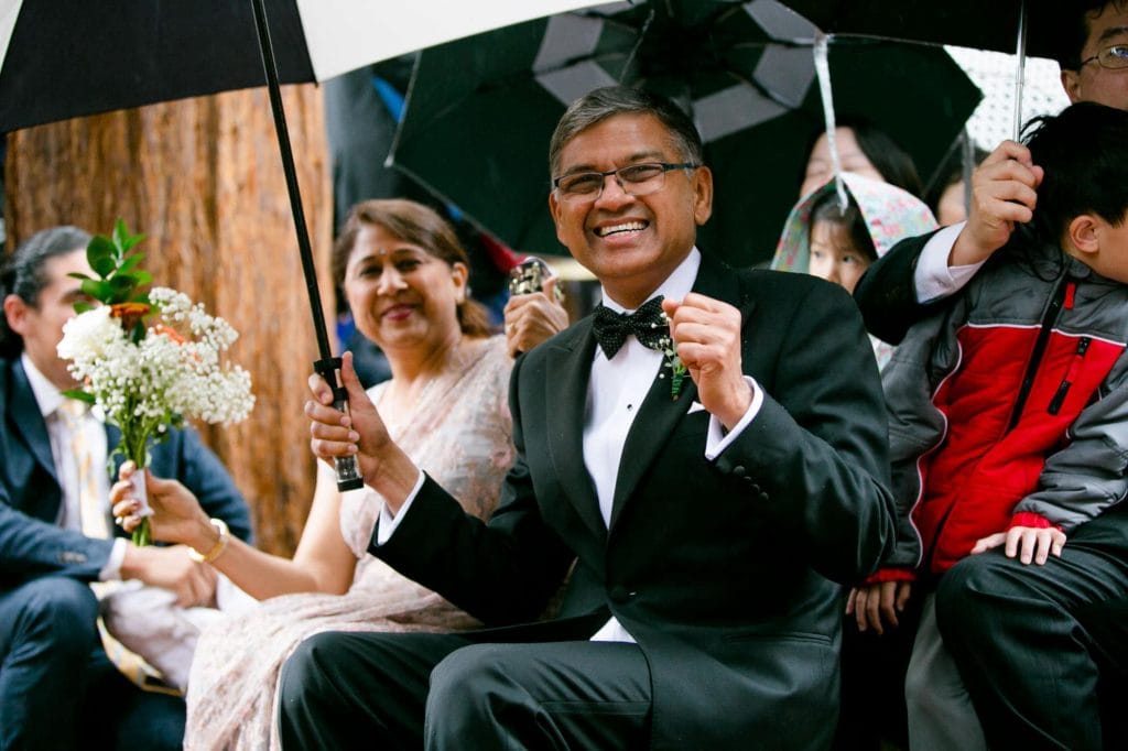 Parents of the groom celebrating and holding umbrellas during the rainy ceremony