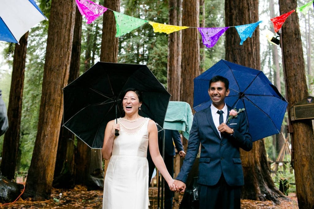 Bride and groom holding umbrellas looking out at their family and friends during ceremony