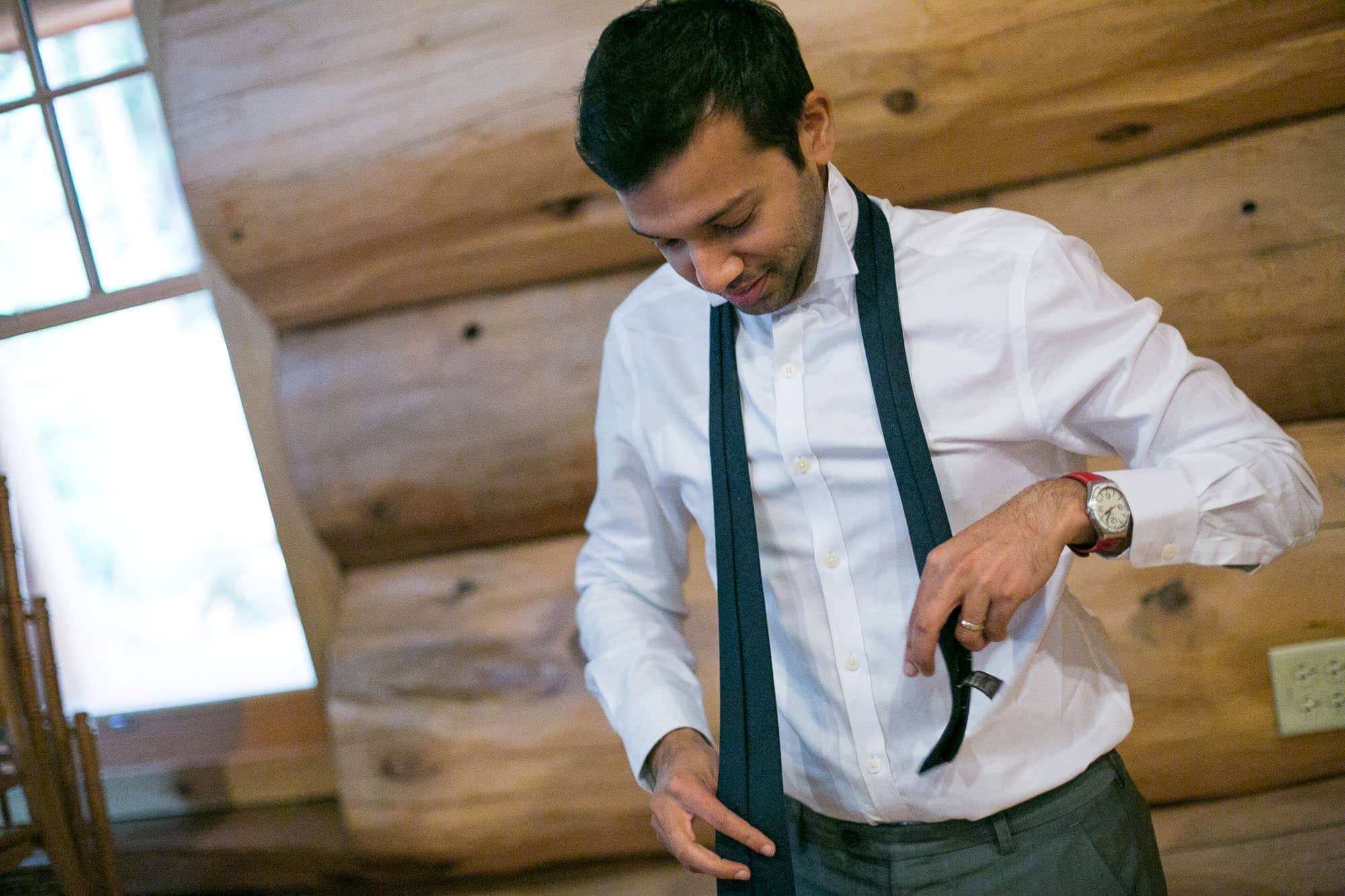 A groomsman tying his tie in a cabin