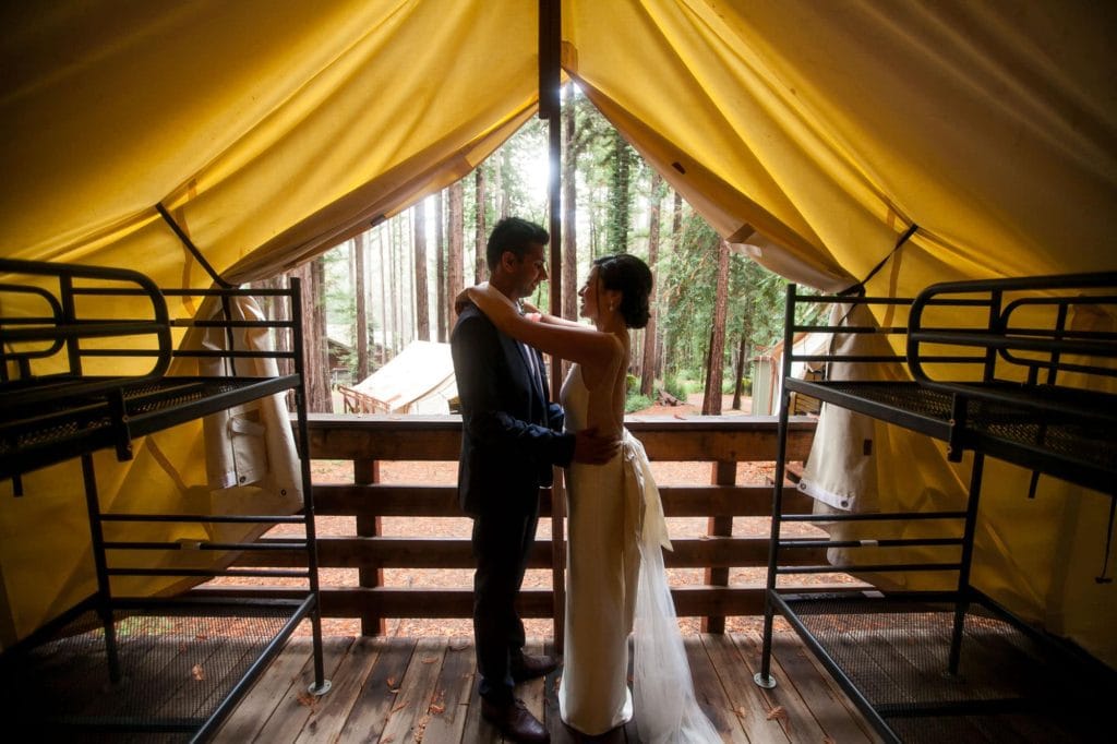 Bride and groom in a tent in the woods hugging