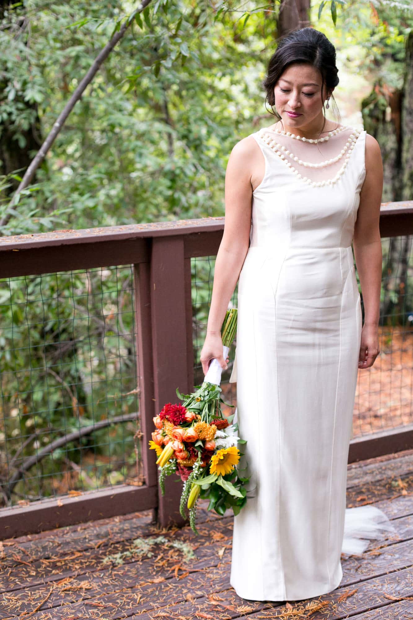 Bride standing on a deck in the woods while holding her bouquet