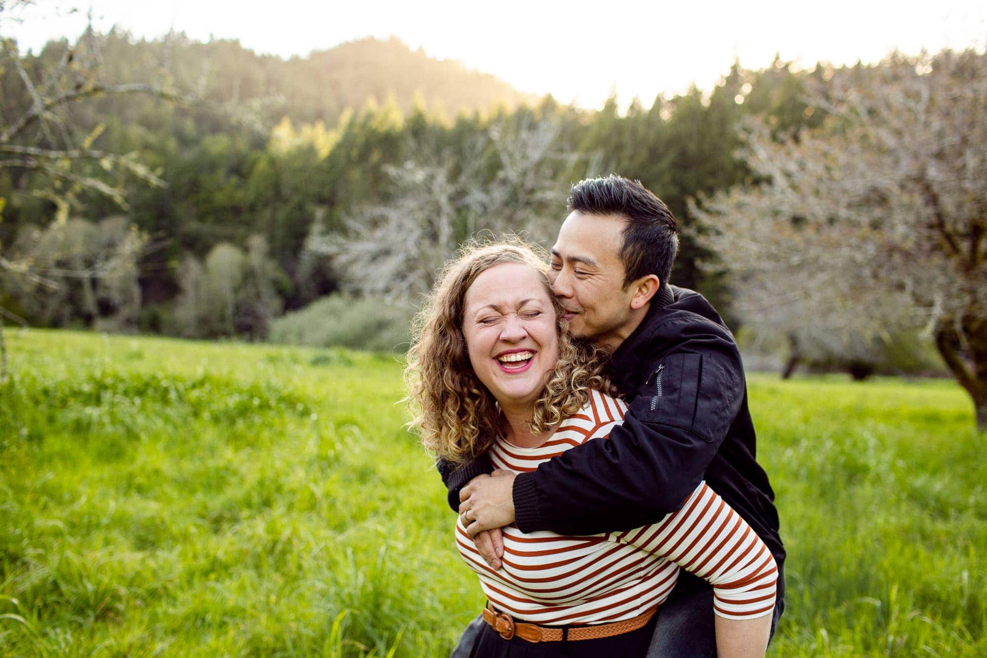 Couple laughing and giving piggy back ride outdoors in a clearing in the woods