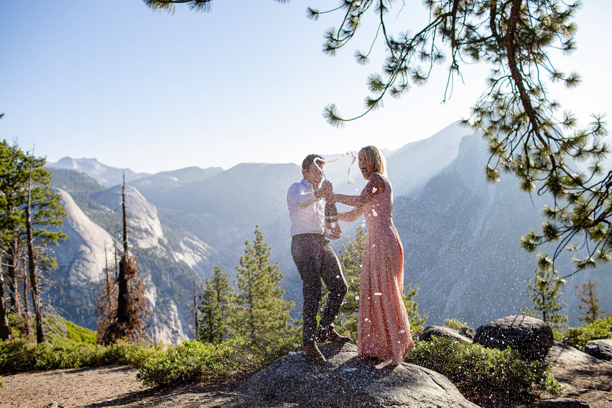 Man and woman popping champagne on mountain top with half dome in the background