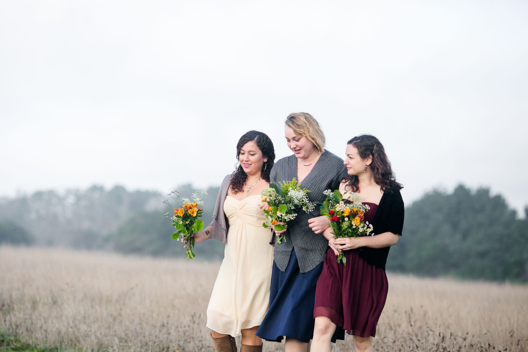 Three women walking through a field holding bouquets