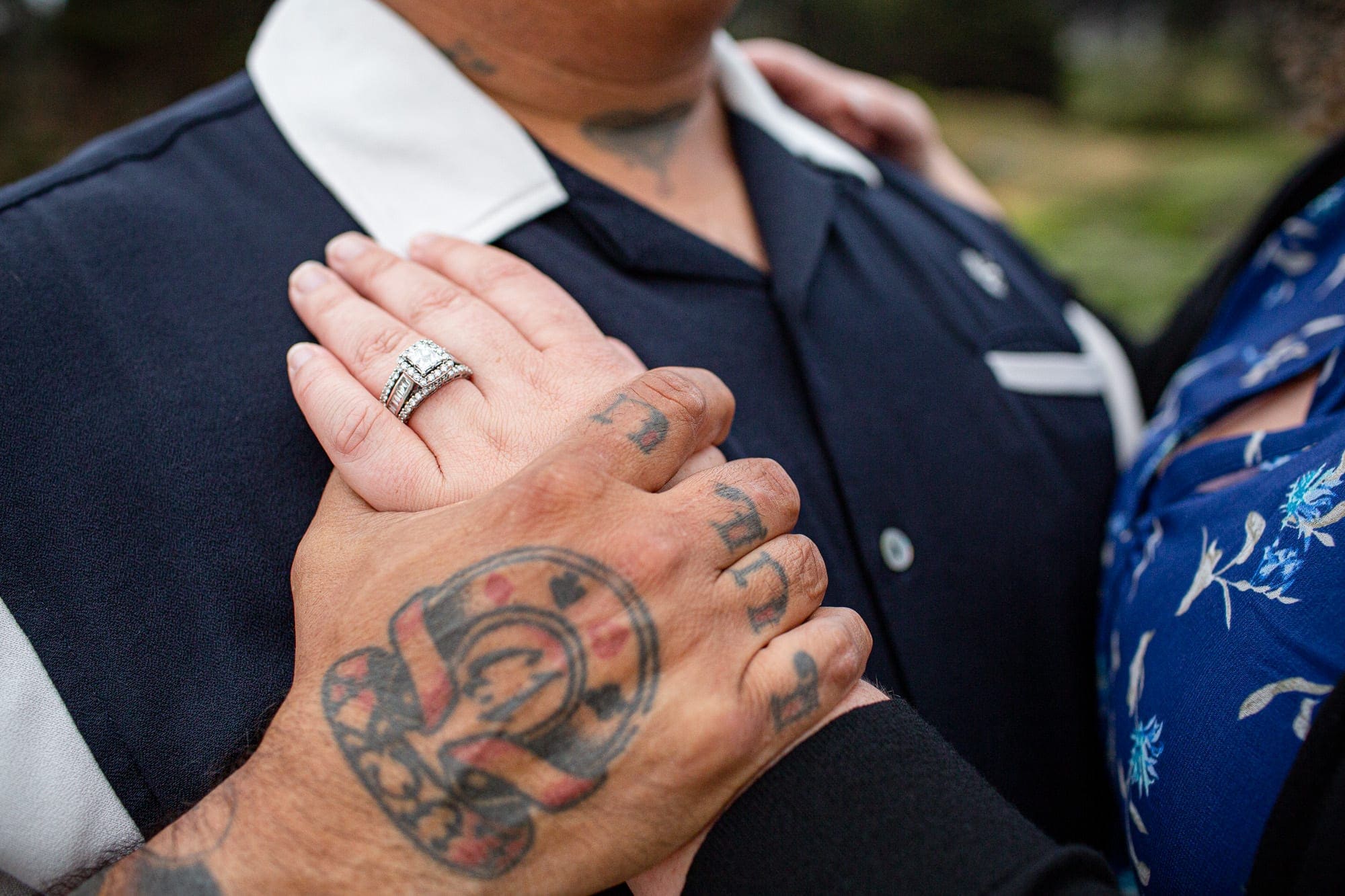 close up of couple holding hands with tattoos and engagement ring
