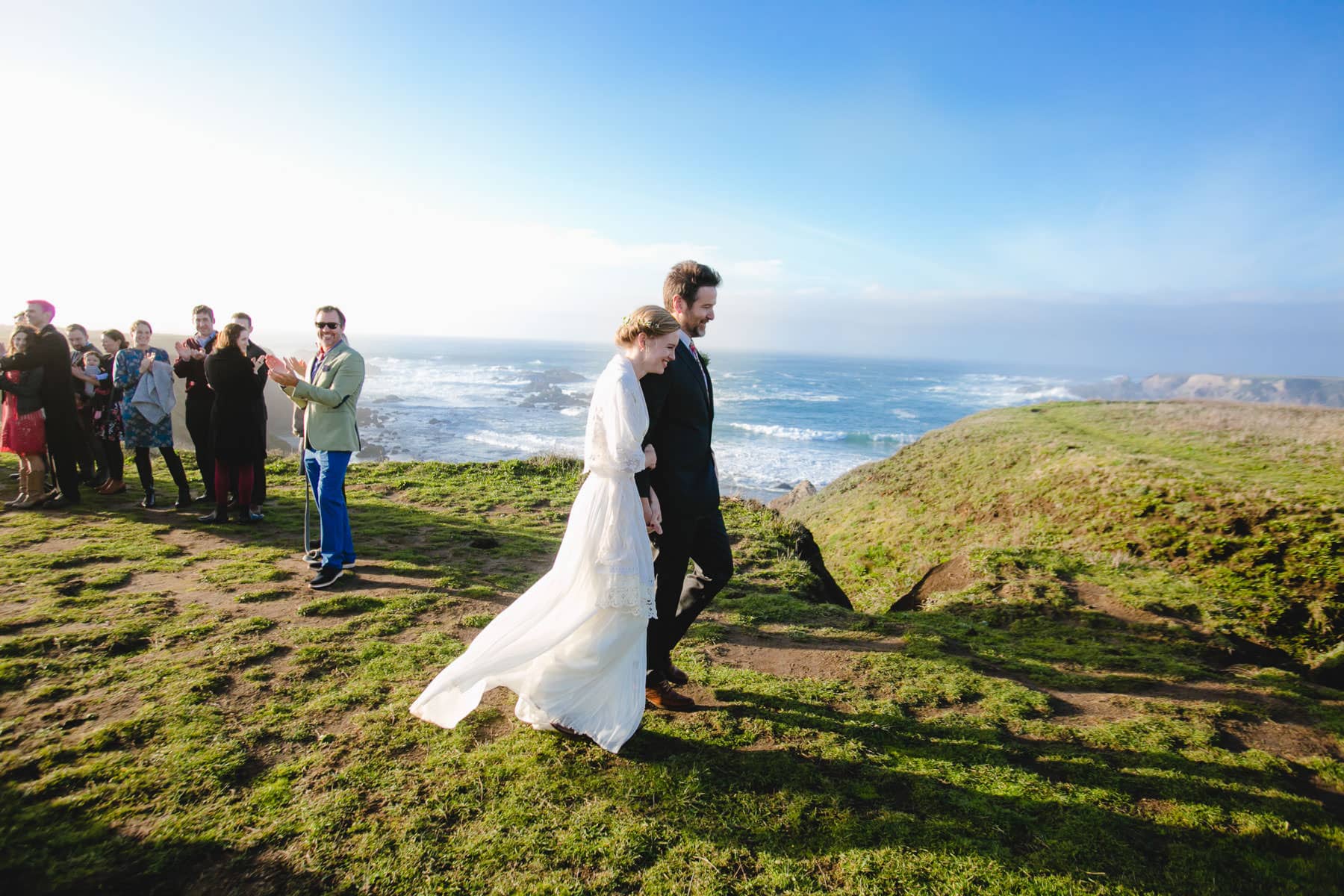 Bride and groom walking away with ocean in the background