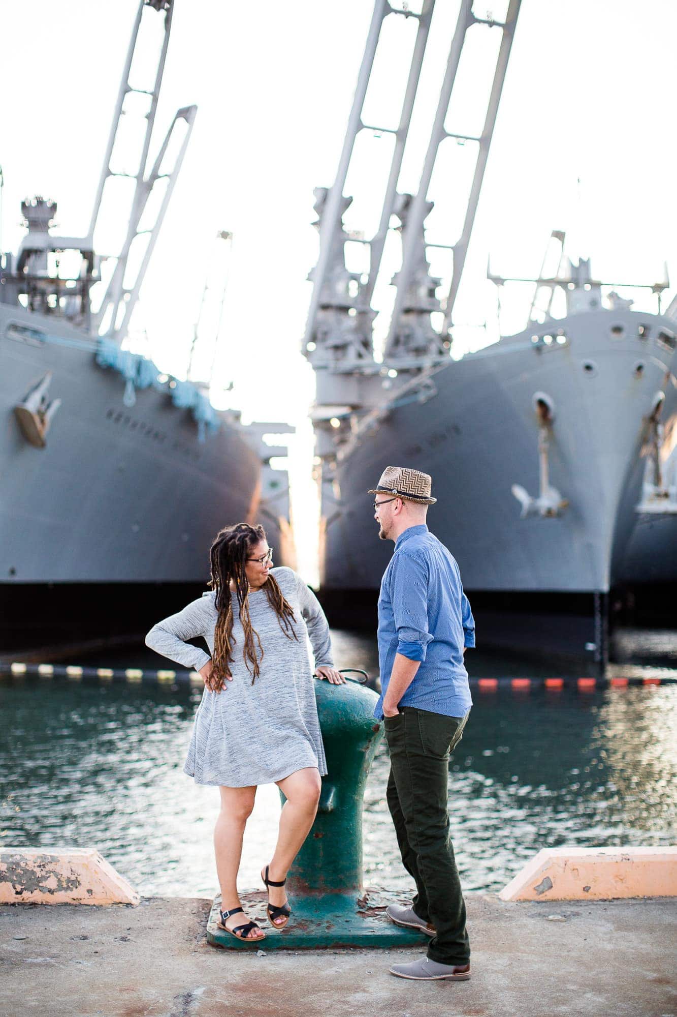 Couple looking at each other standing in front of two navy ships