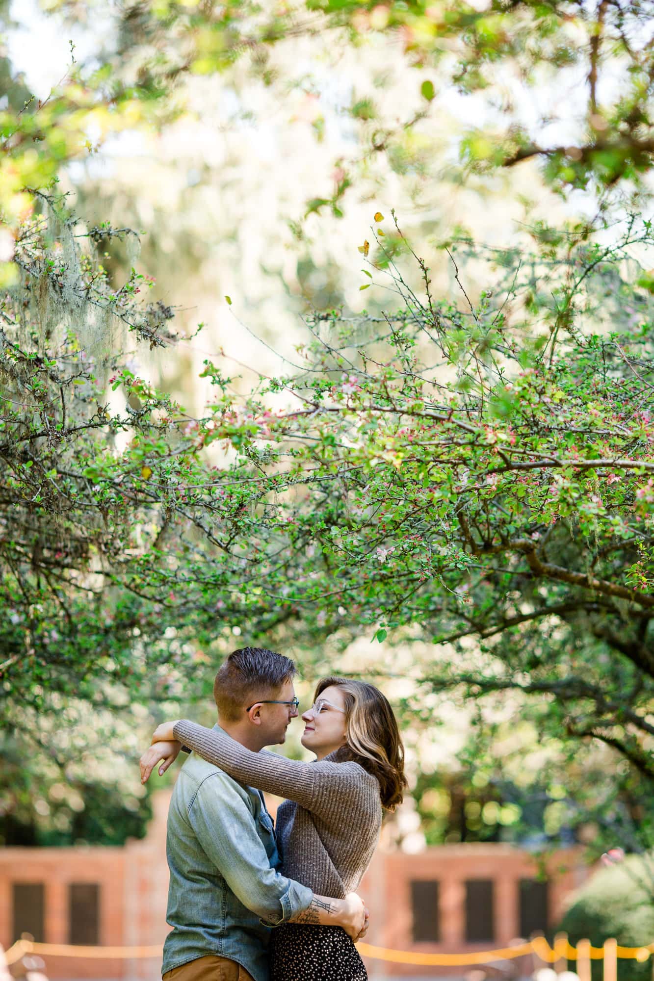 Couple embrace and lean in for kiss with trees behind them