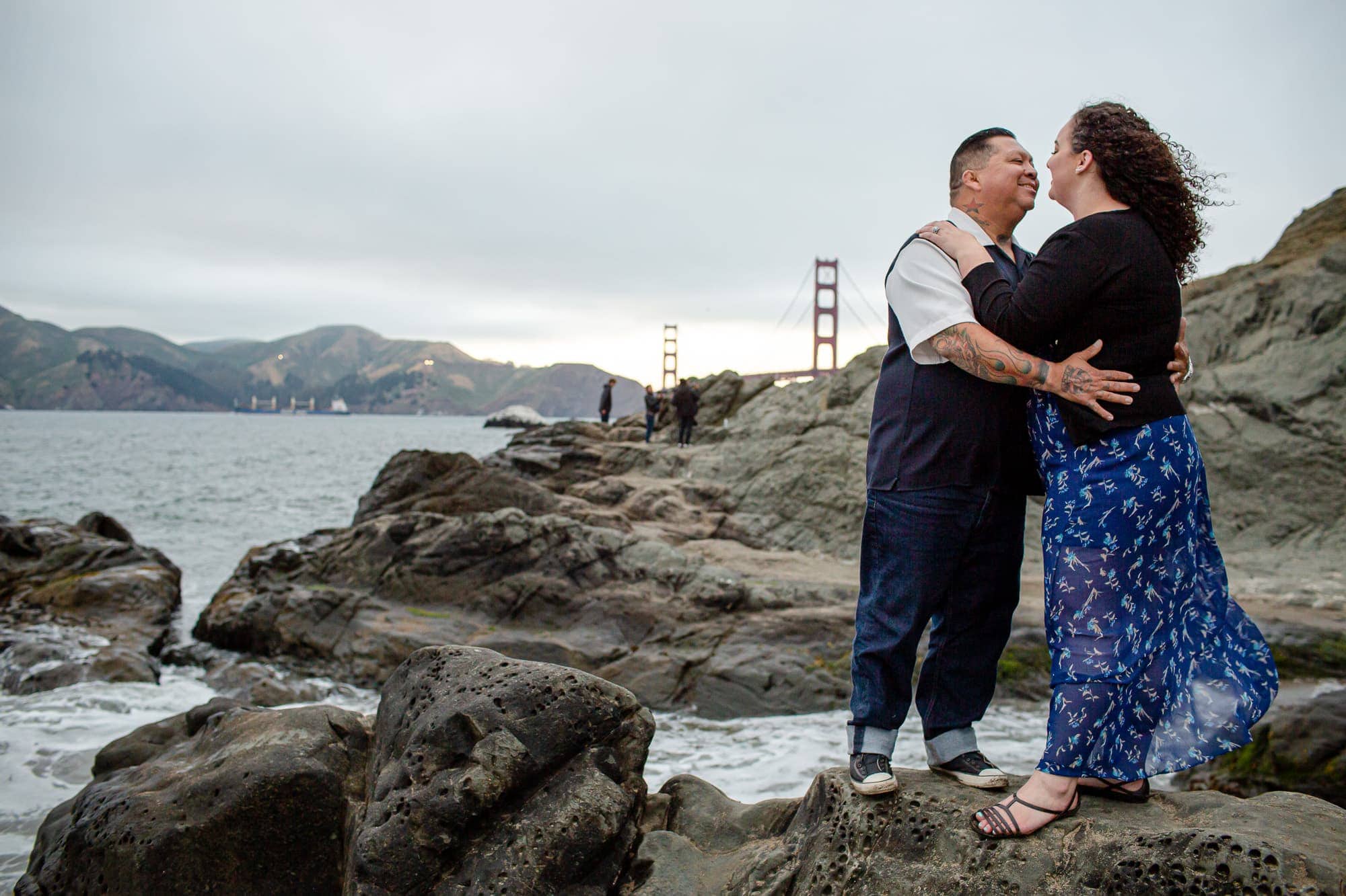 Couple hugging while standing on rocks in front of Golden Gate bridge