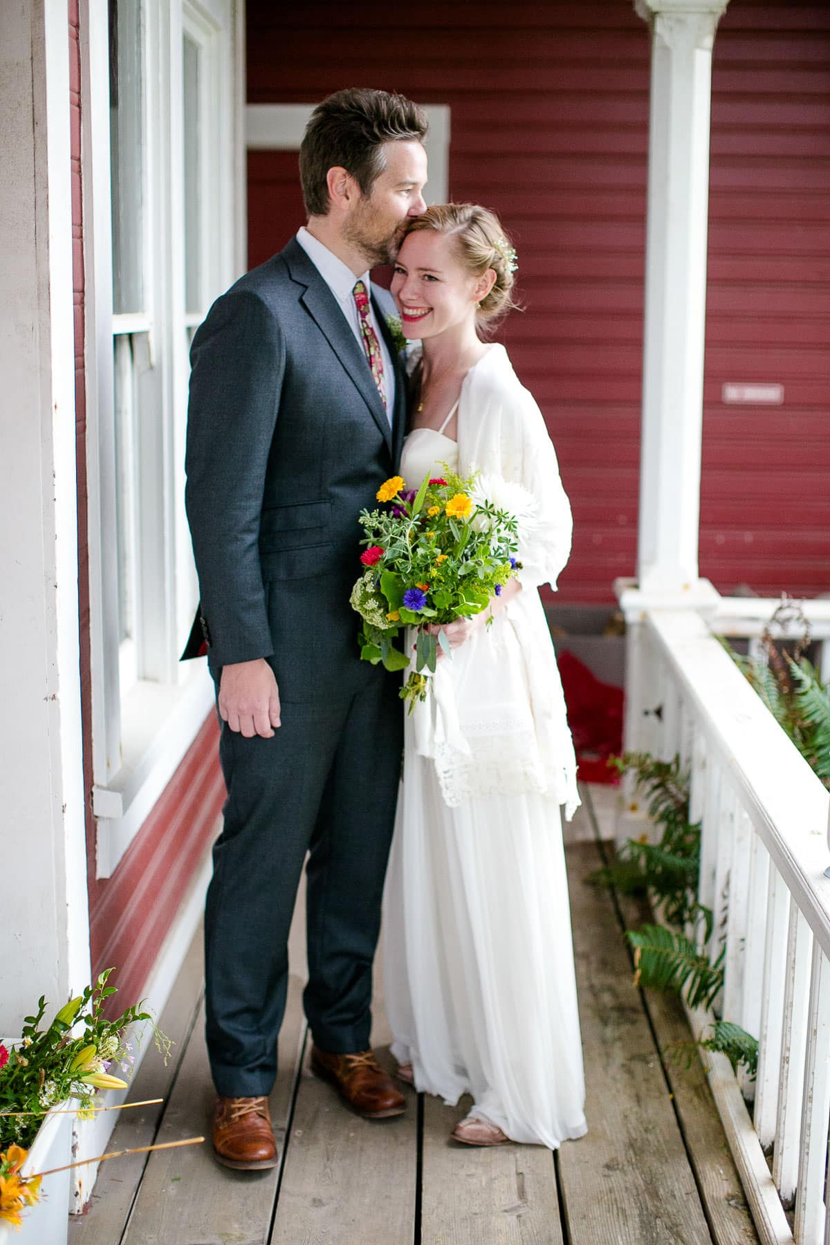 Groom and bride on porch of red house in wedding clothes