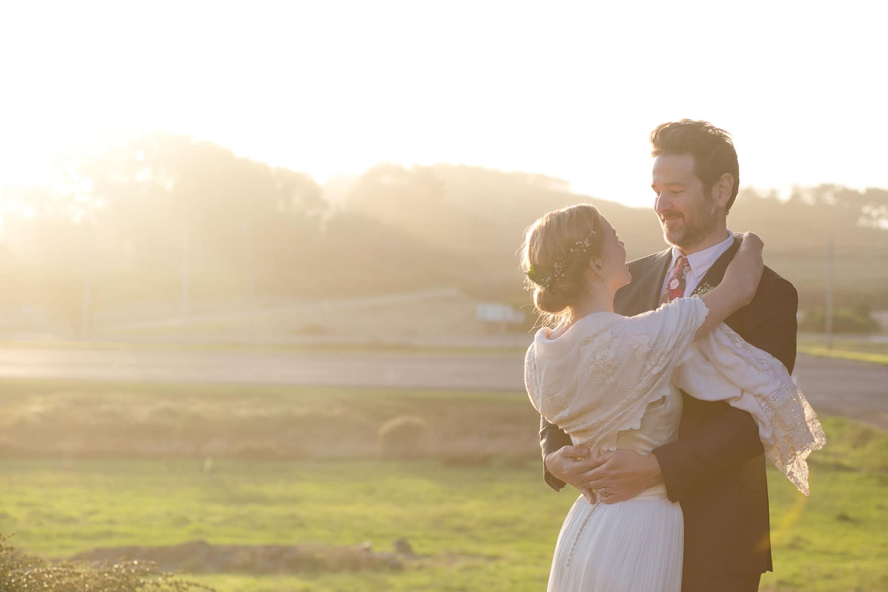 Bride and Groom hugging outside on grassy hill during sunset
