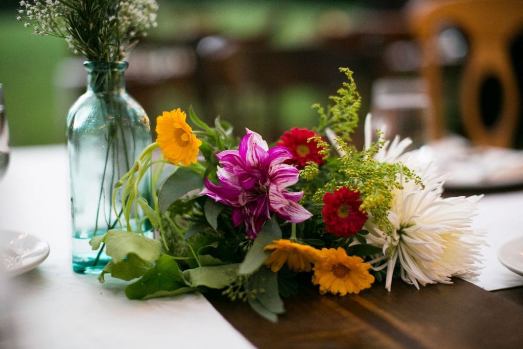 yellow pink and red arranged flowers on a wooden table at a wedding