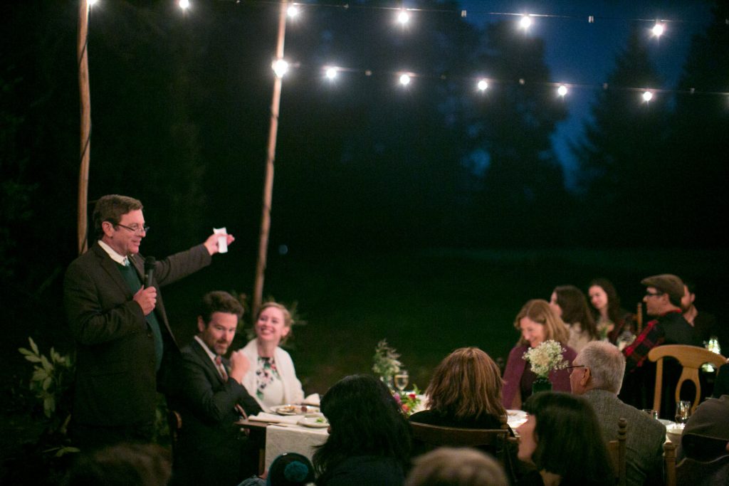 Man gives toast to bride and groom at outdoor wedding a night