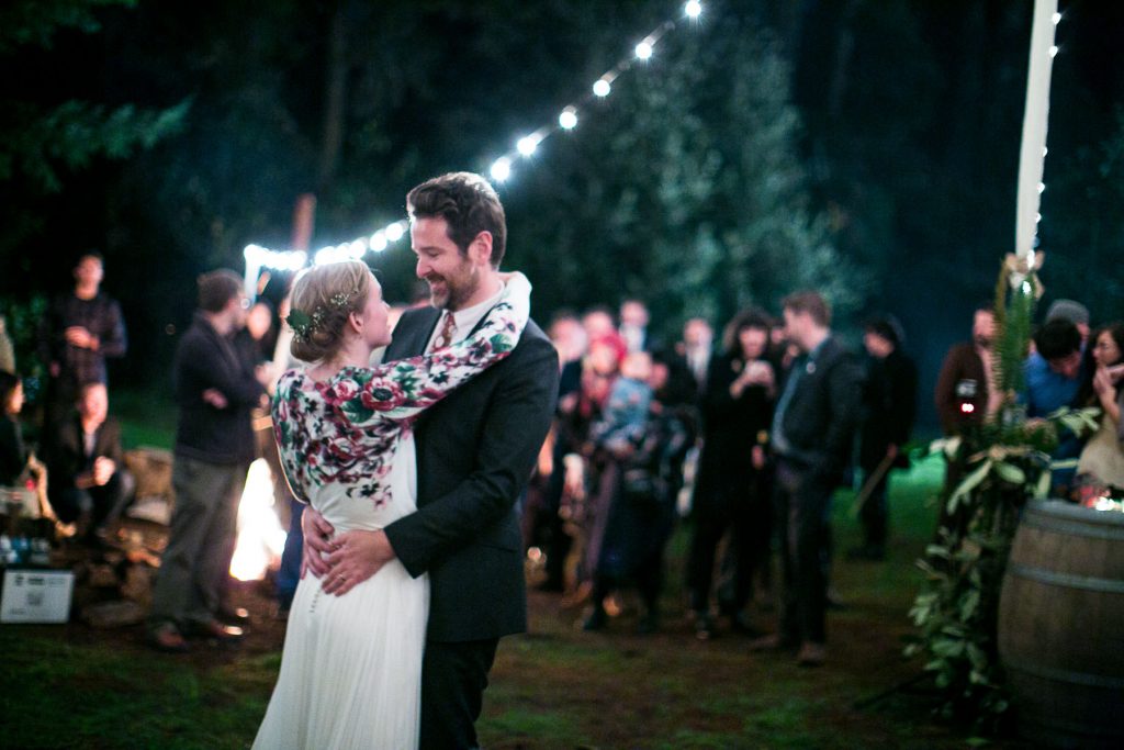 Groom and bride dancing outdoors at night with market lights on a maypole in the background