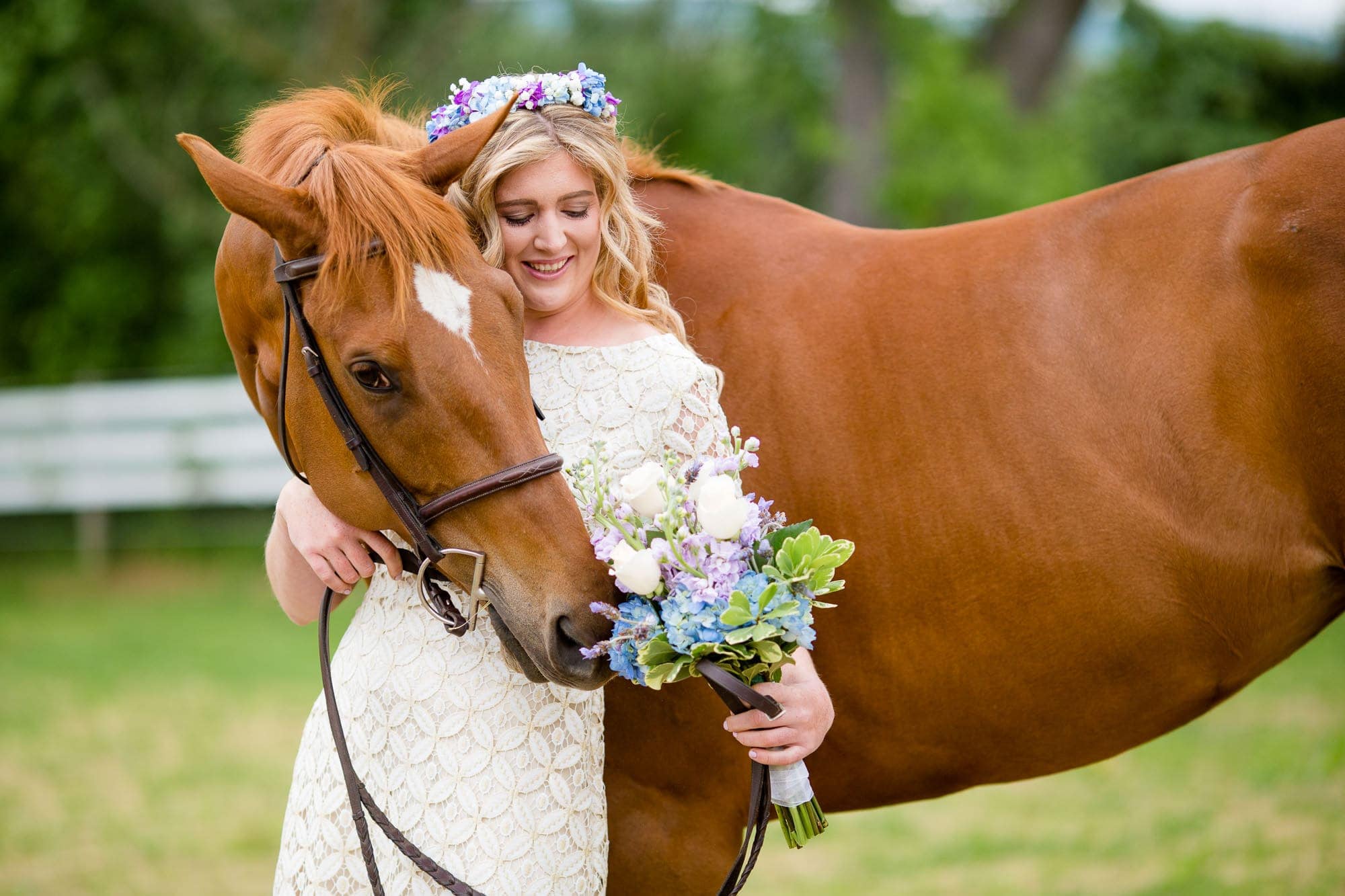 Brown horse nbext to a woman in a white wedding dress and flower crown trying to eat the brides bouquet
