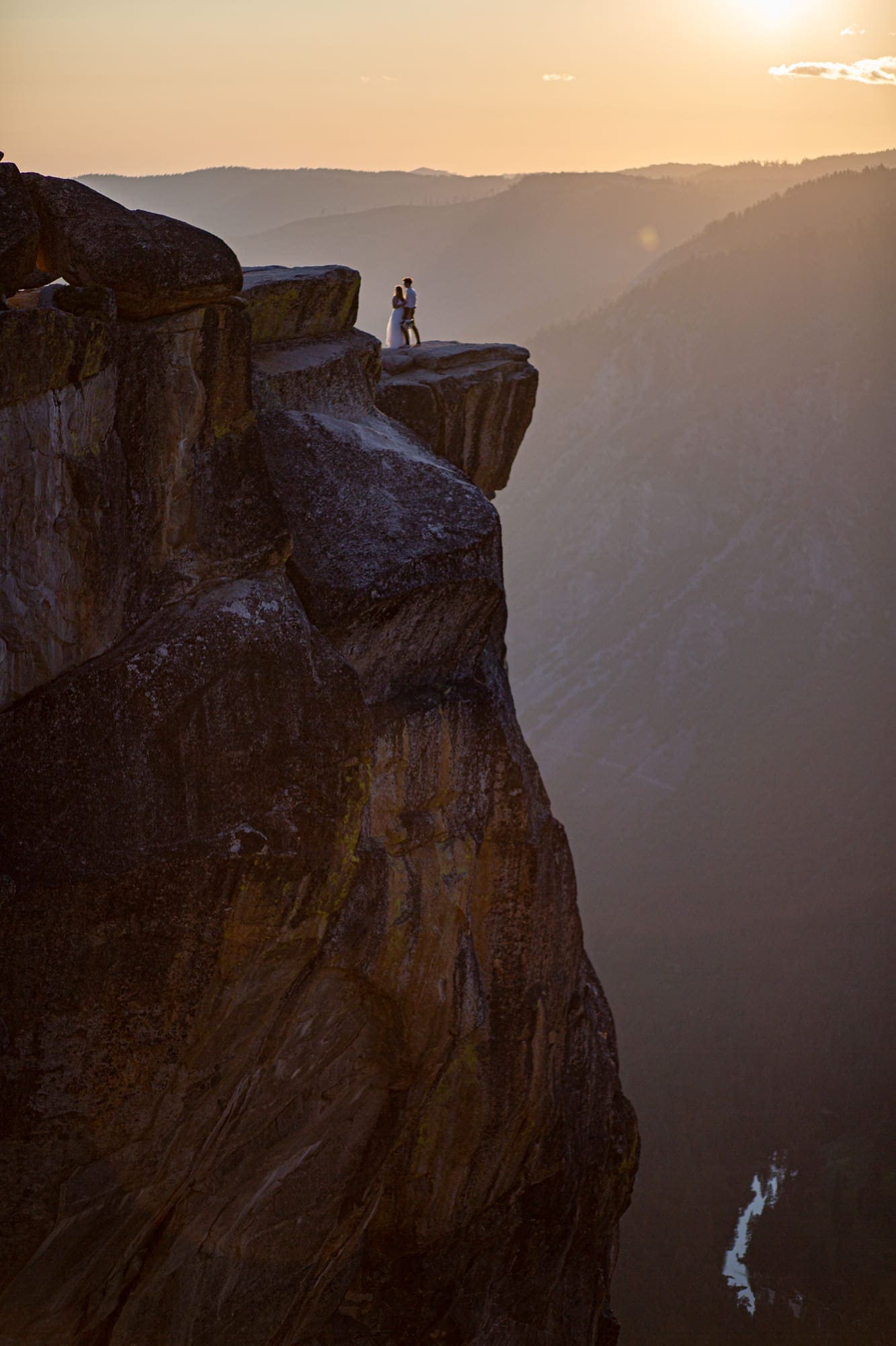 Bride and groom standing on a rocky outcropping silhouetted at sunset in Yosemite after and adventure elopement