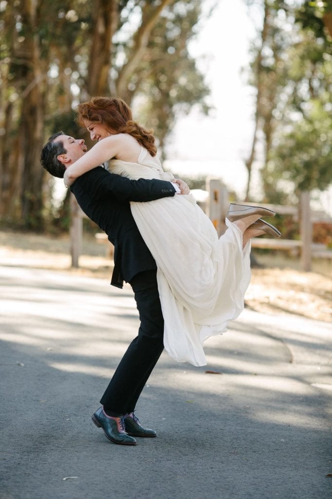 Husband and wife celebrating as groom picks up bride outdoors in Northern California
