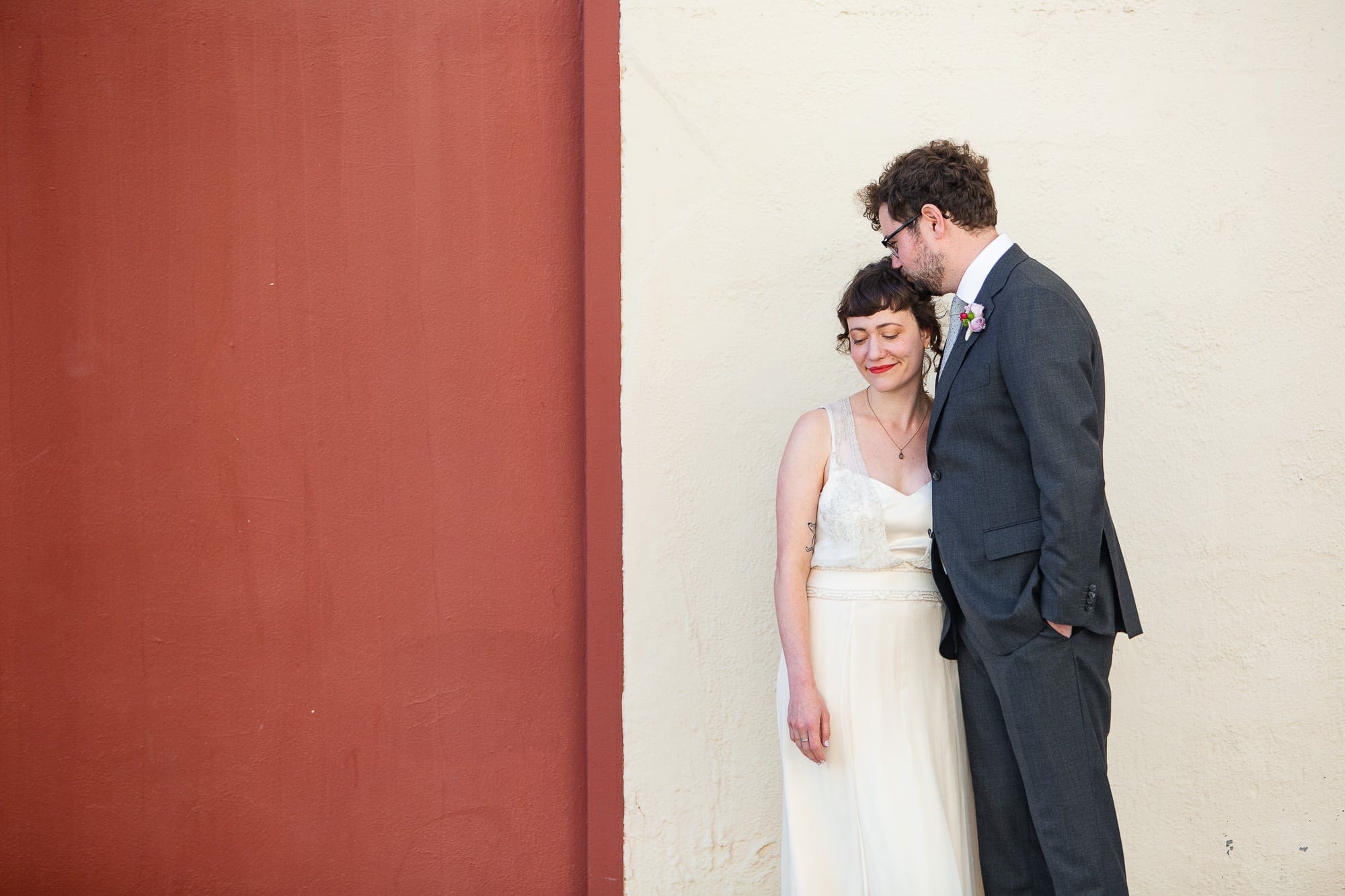 Modern bride and groom in front of an urban red and white wall before the wedding