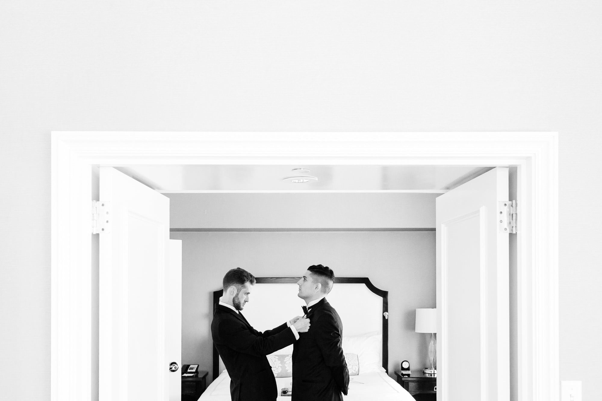 Best man helps groom adjust his bowtie in Hotel room in San Francisco