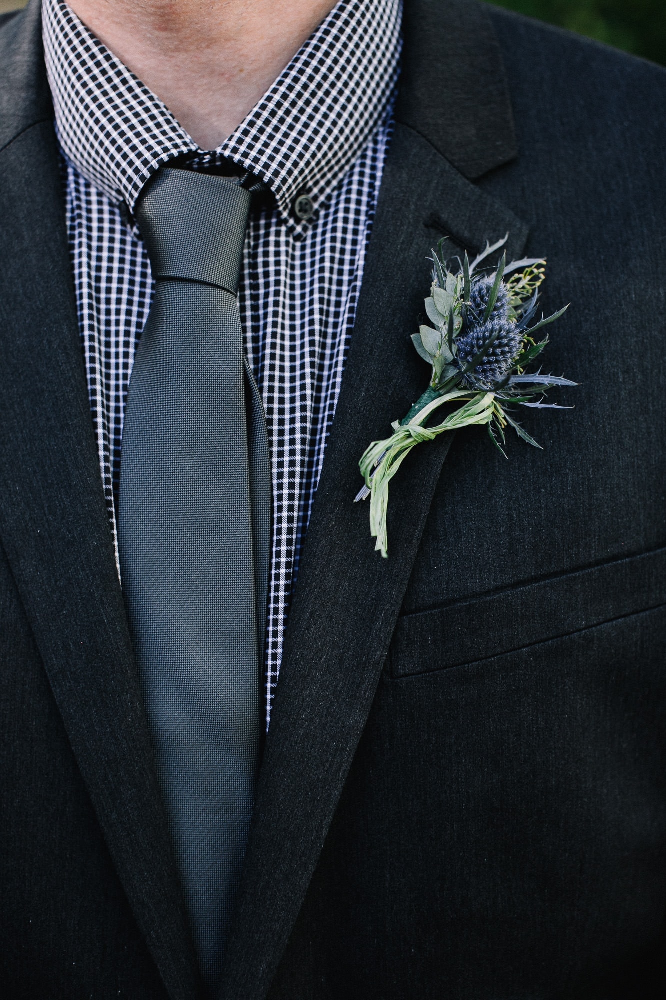 Thistle boutineer with a black and white checkered shirt and grey tie detail photo of groom