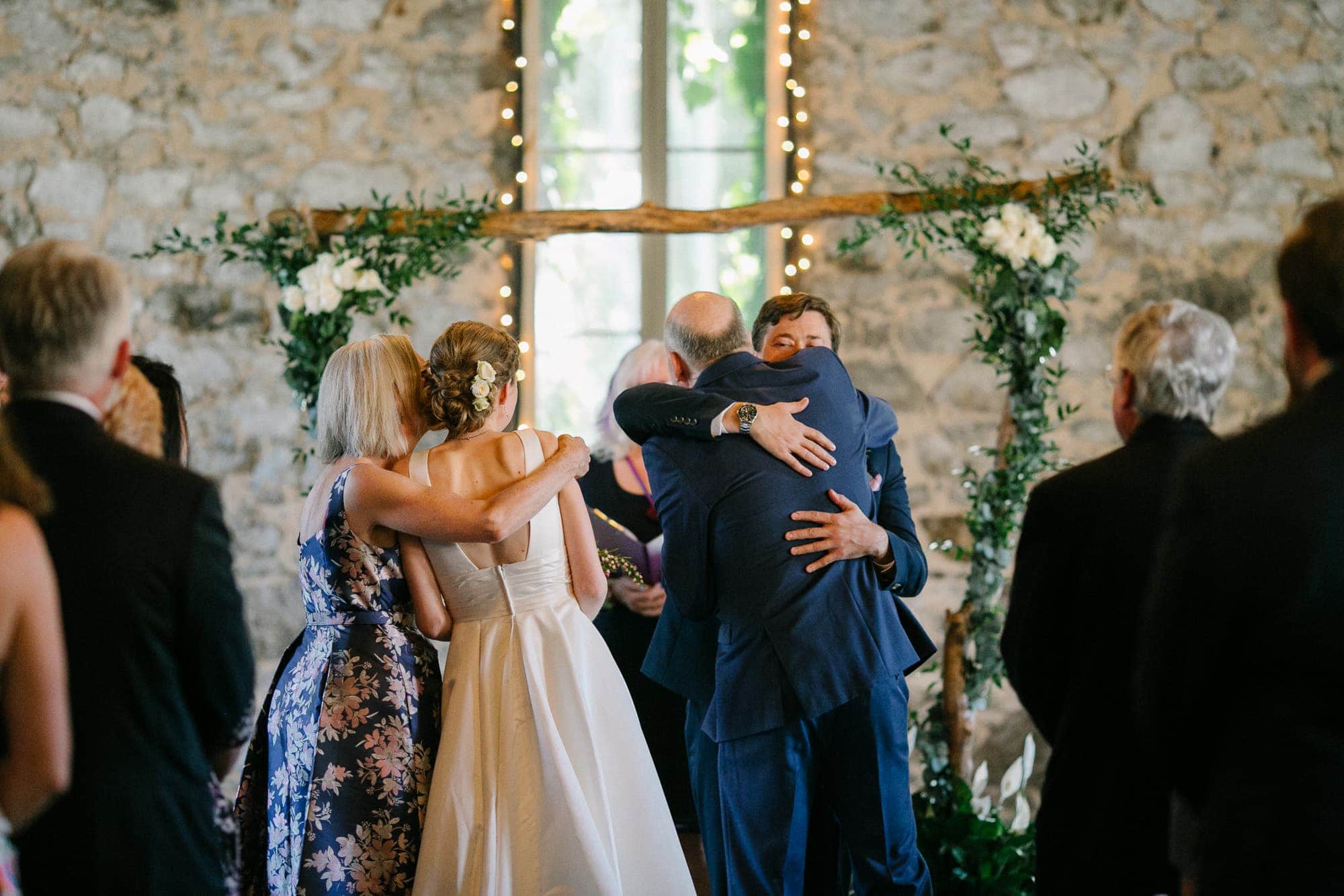 Bride and groom hugging their parents before indoor wedding ceremony in Nevada City with floral arch in background