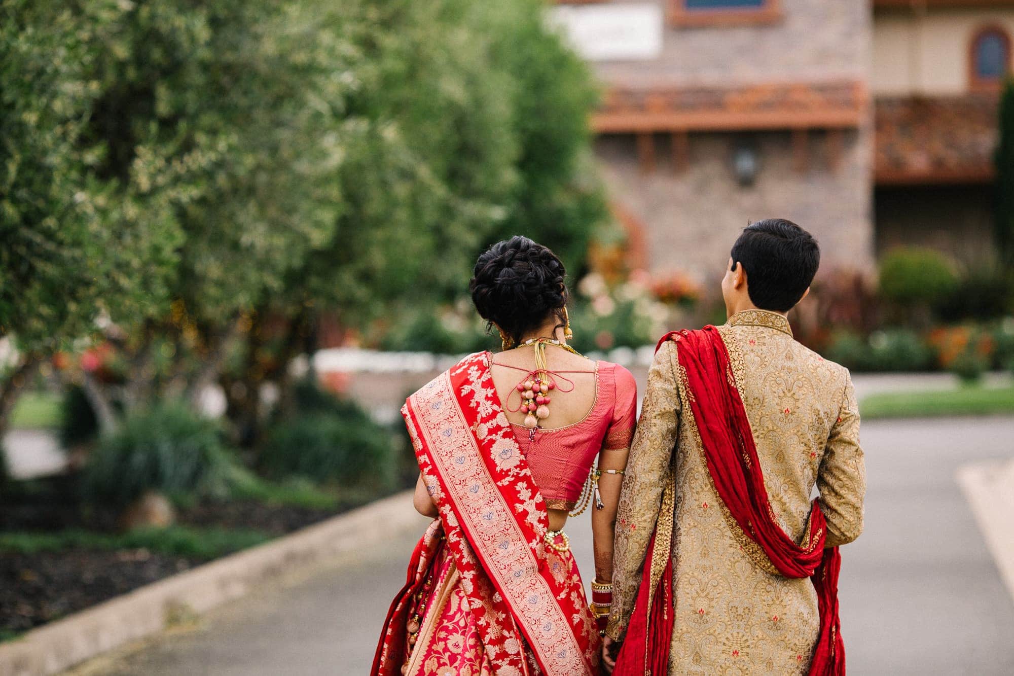 Indian bride and groom in red traditional clothes walking back to their winery venue in Pleasanton