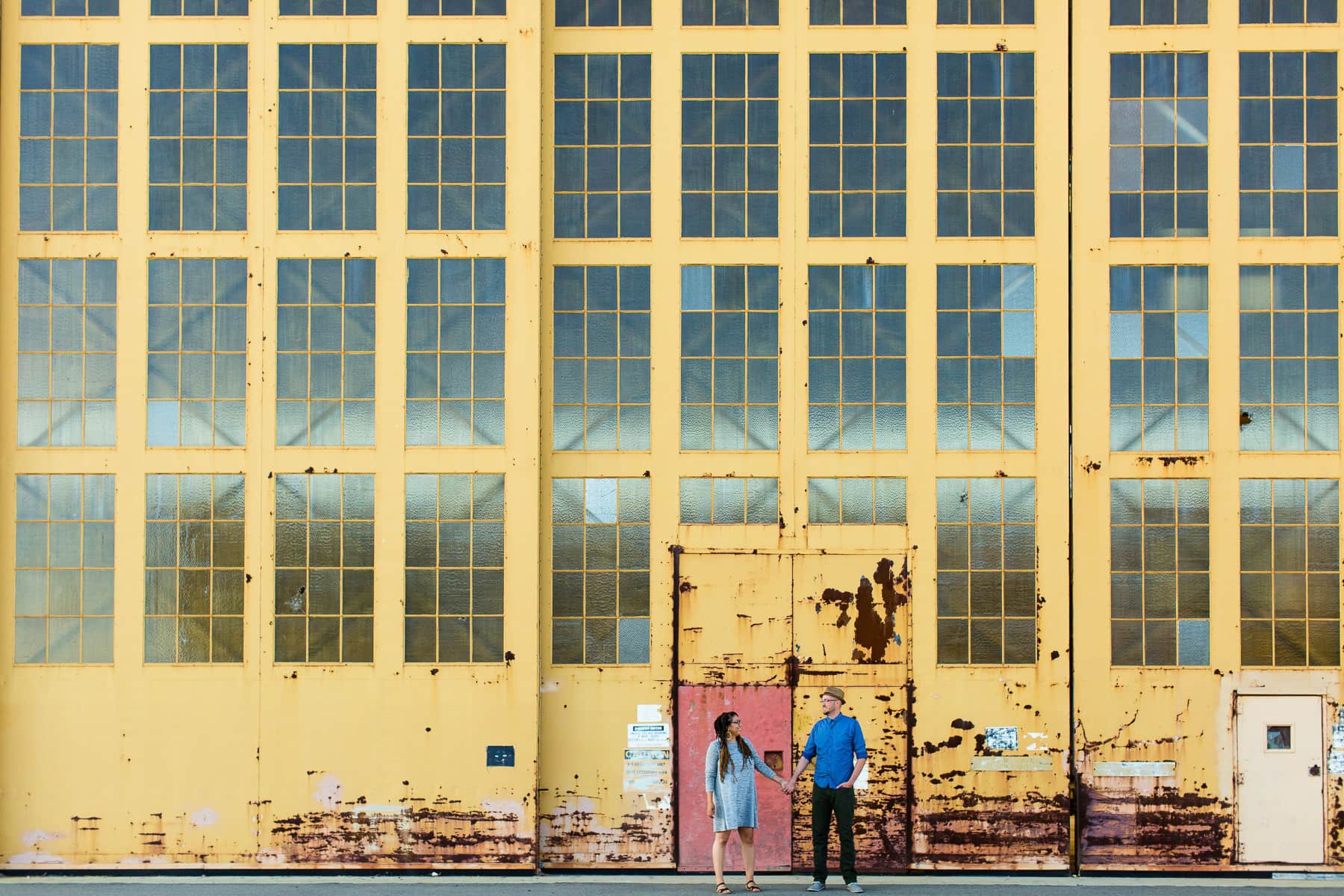 Woman and man stand in front of dilapidated yellow warehouse