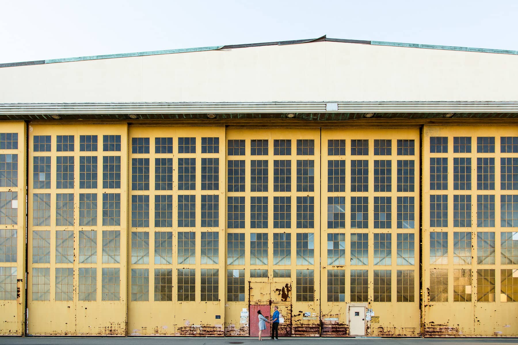 Two people stand in front of Giant yellow windowed warehouse walls
