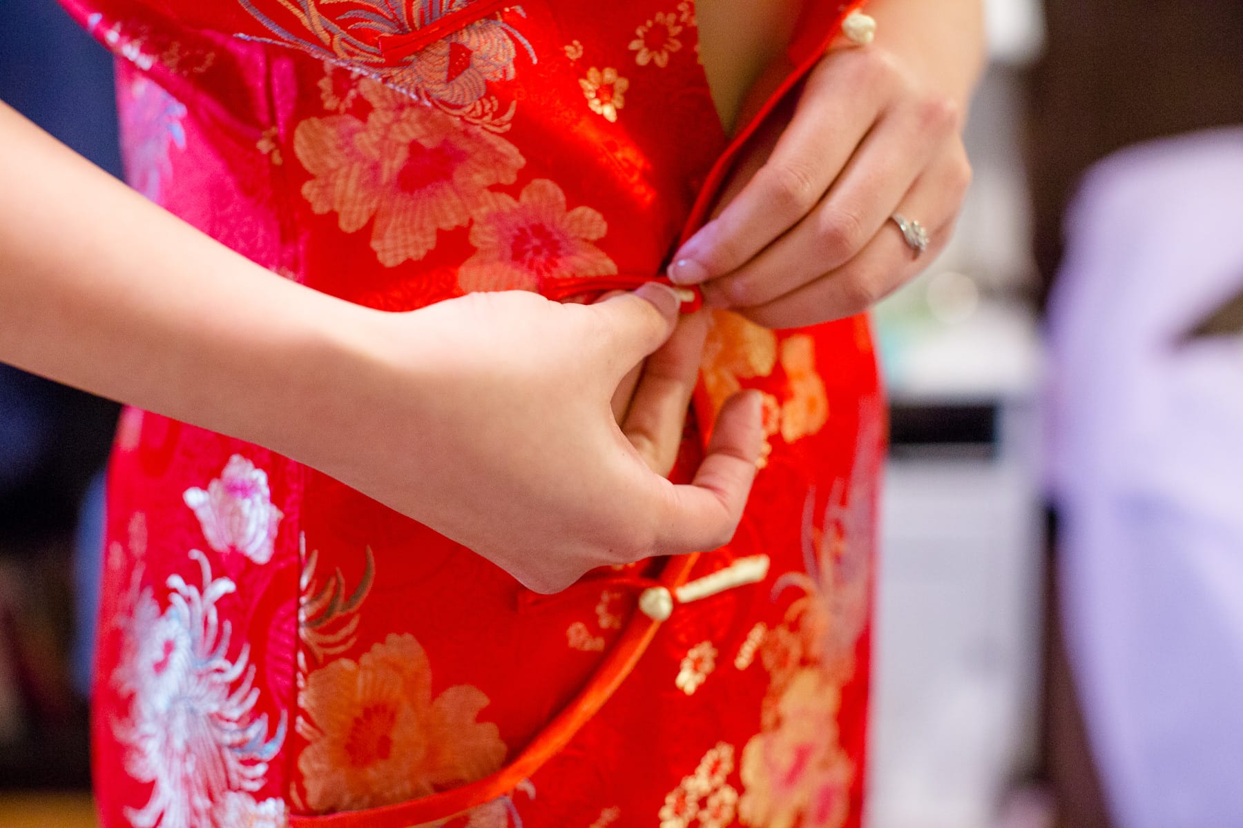 detail of brides hands buttoning up her qipao
