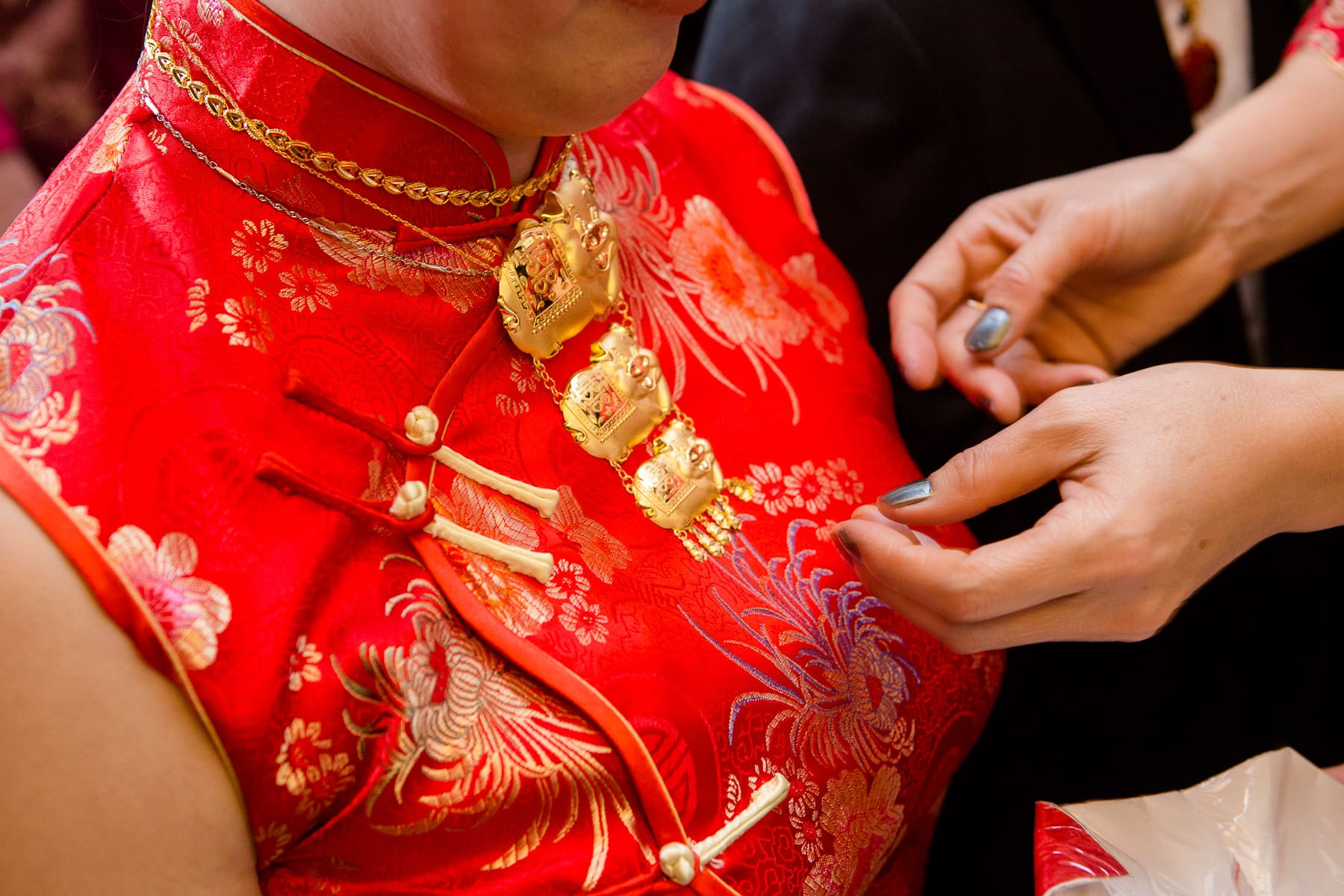 Bride in red dress receiving golden pig necklace during tea ceremony