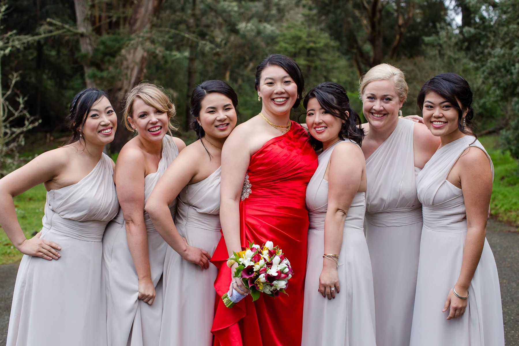 Bride in red dress standing with bridesmaids outdoors in the woods