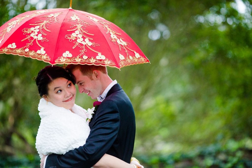 Bride and groom cuddling under red umbrella