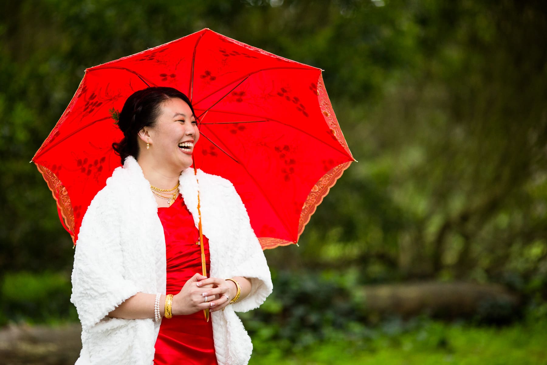 Bride in red dress with red umbrella laughing