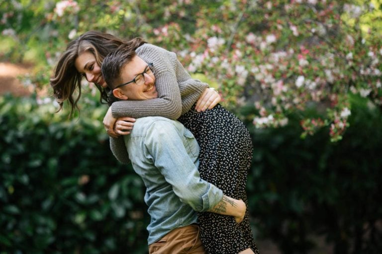 Man picking up and twirling woman around while smiling in green floral garden
