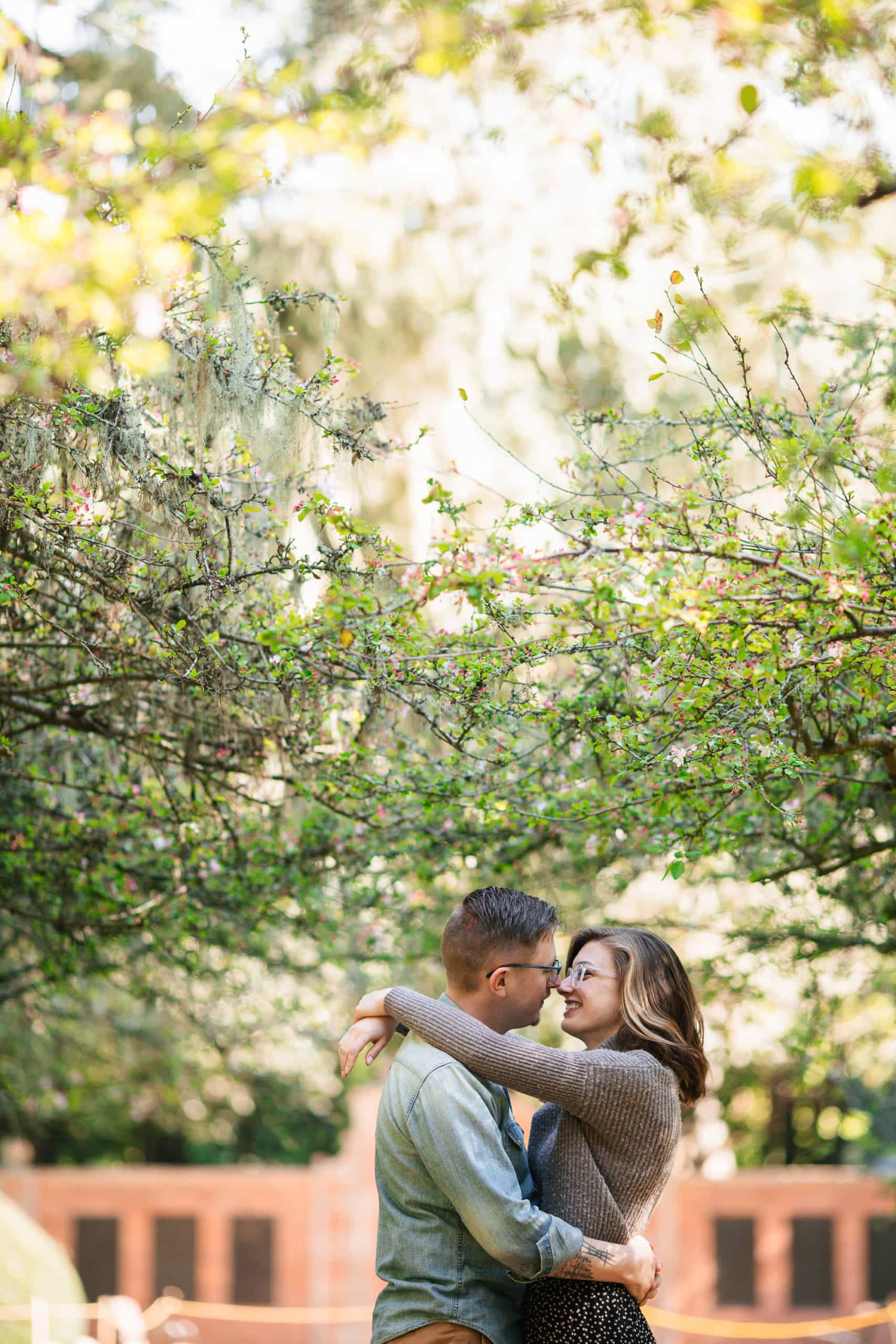 Couple embracing in front of trees and bricks in a garden