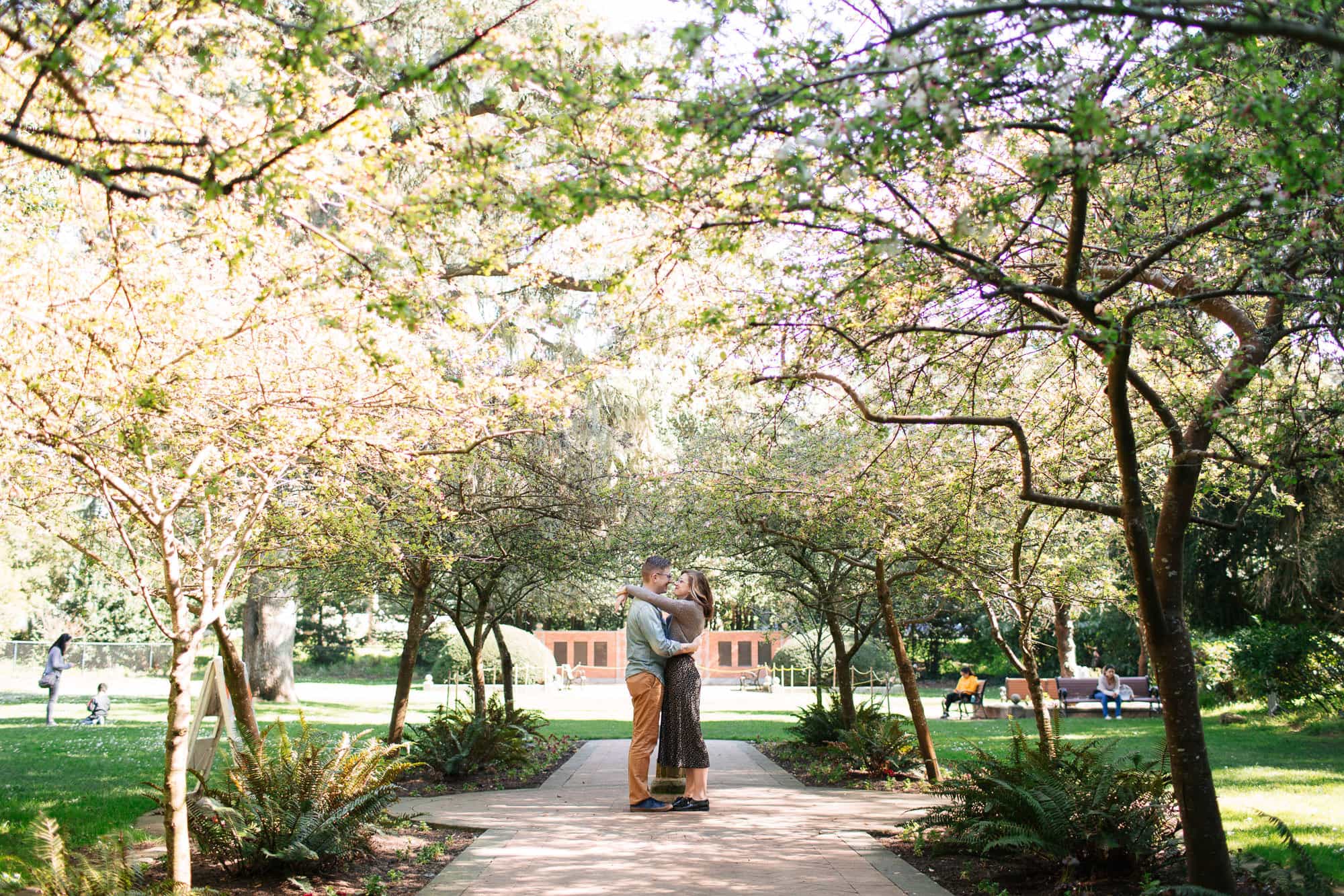 Engaged couple hugging underneath trees in a lush garden