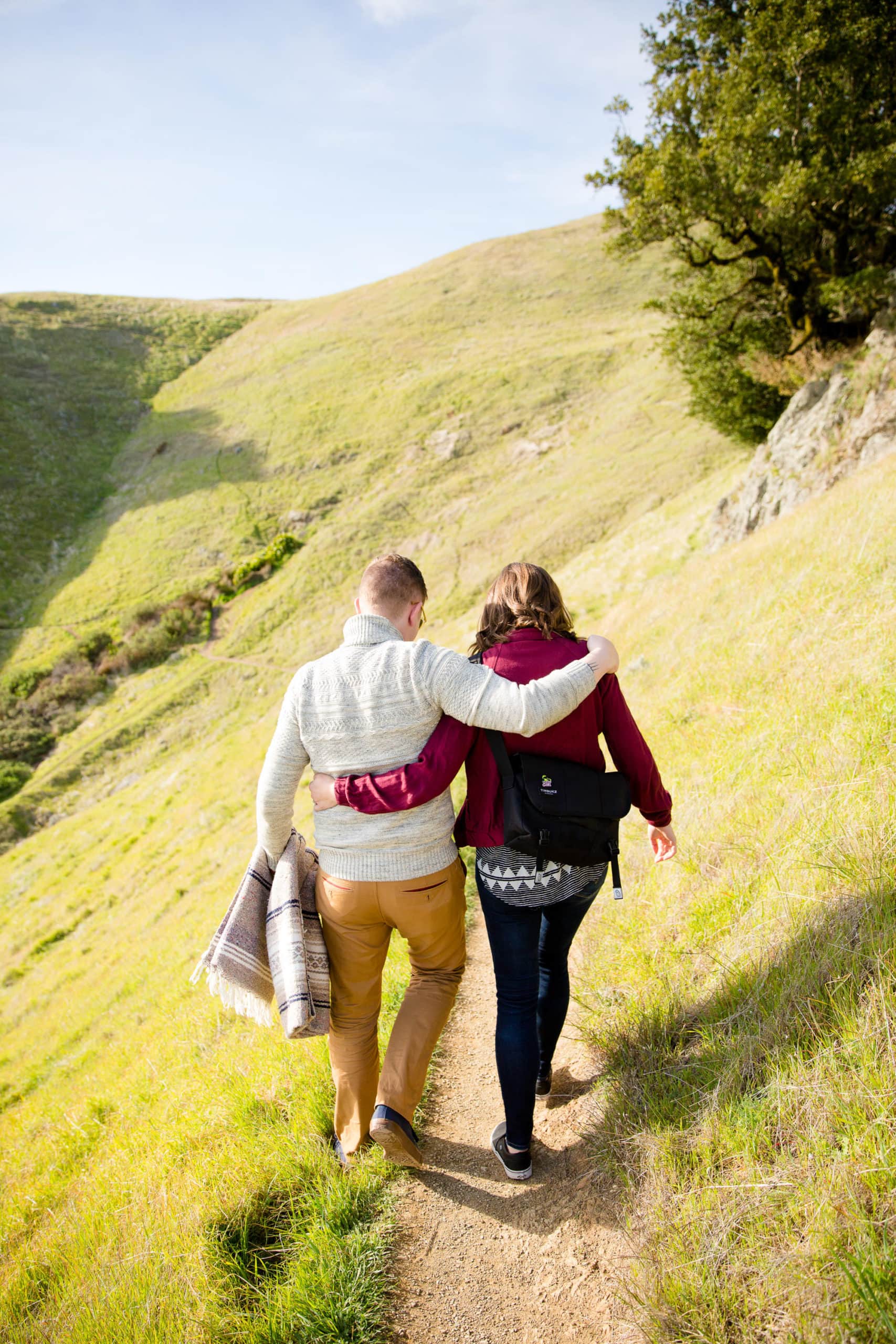 Walking couple with arms around each other on a path on a grassy mountain