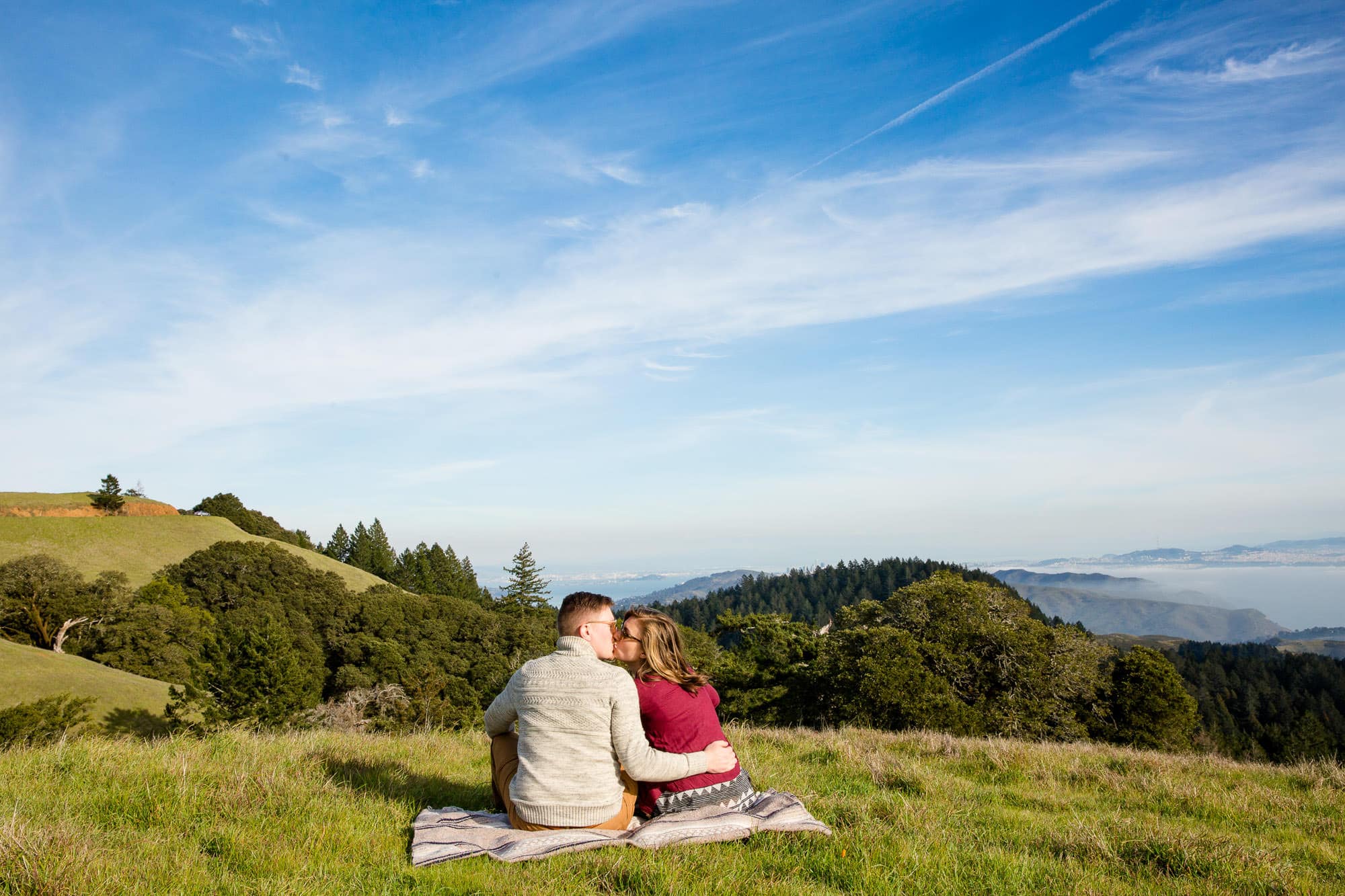Sitting couple on a blanket on top of a grassy hill
