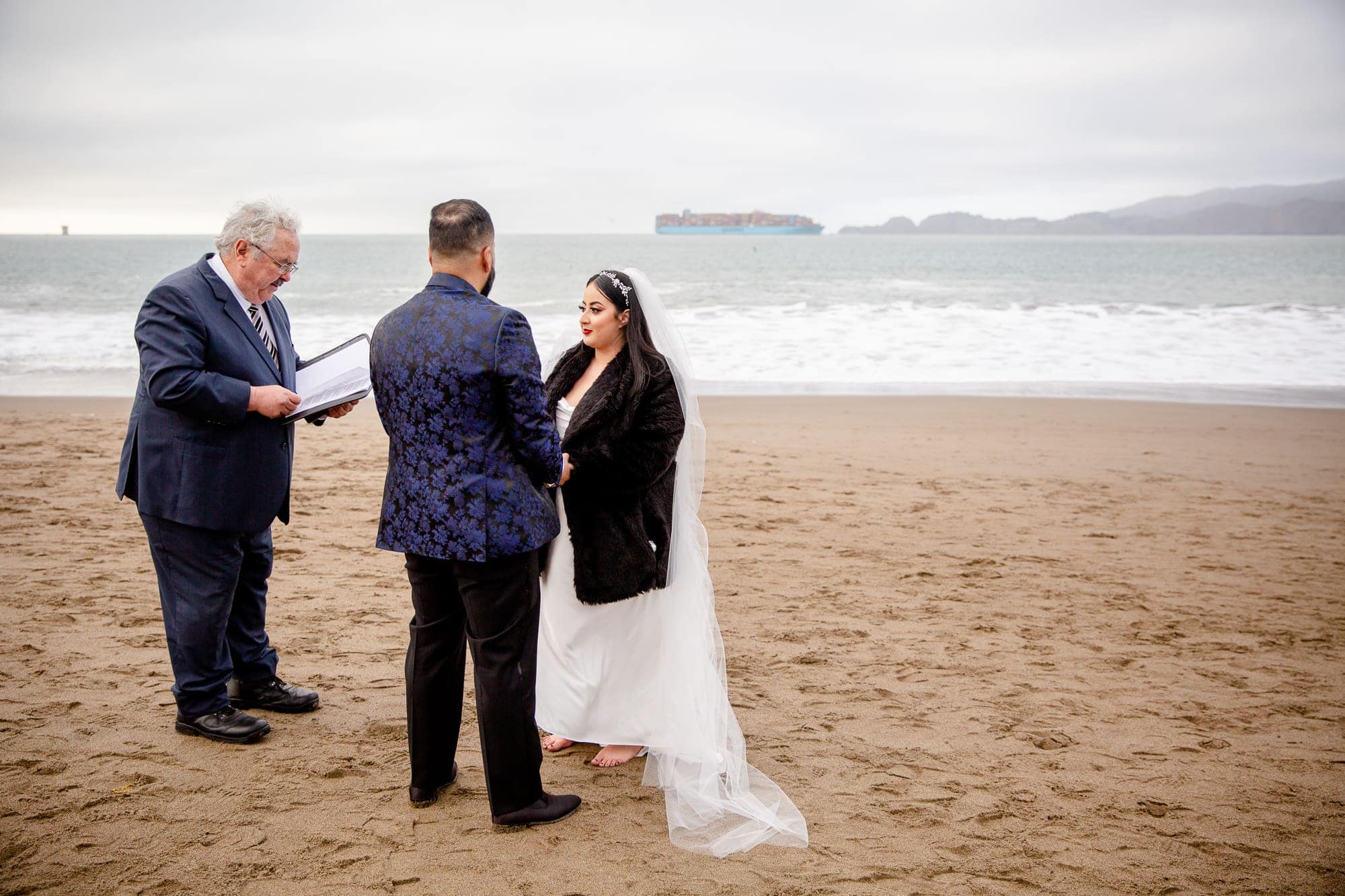 Couple and their officiant perfoming a wedding ceremony on the beach at winter