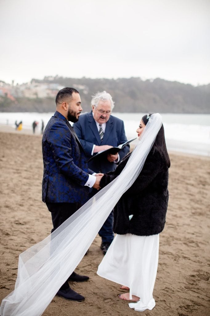 A couple holding hands getting married on the beach in the cold