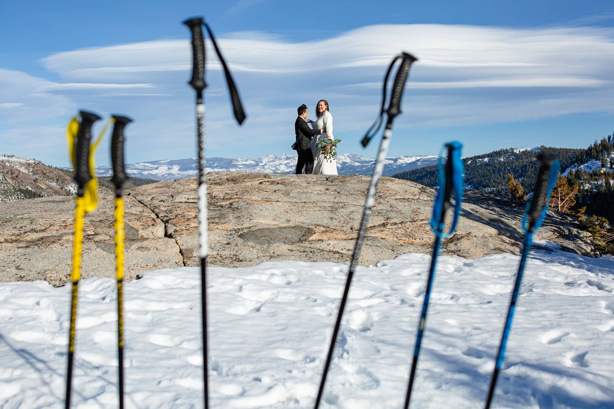 Elopement couple on top of a snowy mountain with snow shoeing poles in the foreground