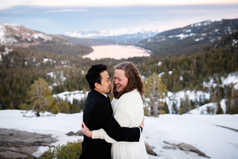 Couple laughing after elopement ceremony in the snow up on a mountain with a lake and snow in the background
