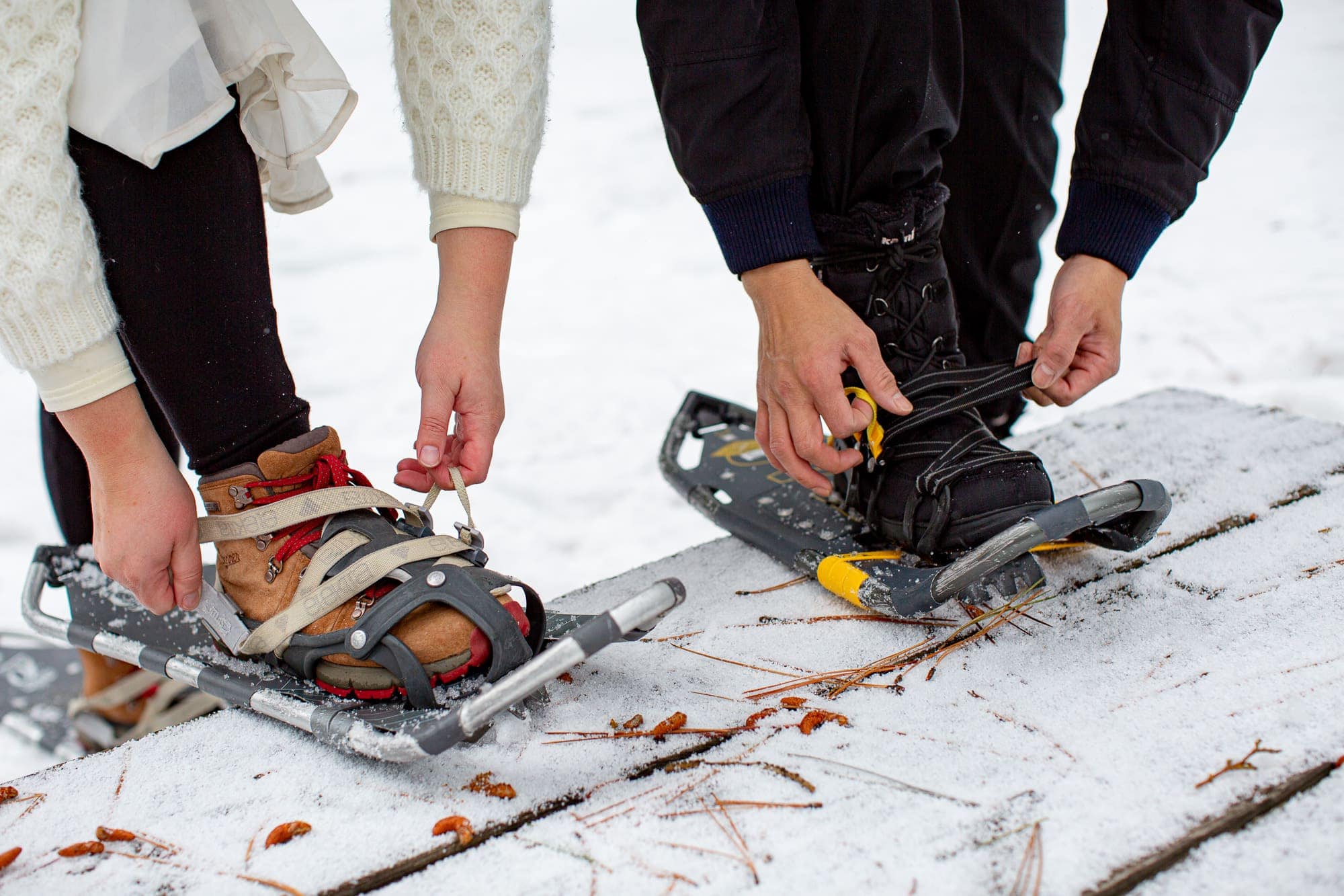 Close up of bride and groom attaching snowshoes to their feet on a snow covered bench