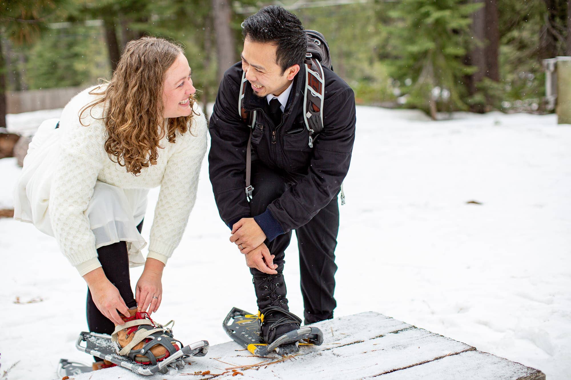 Wedding couple putting on snowshoes and looking at each other
