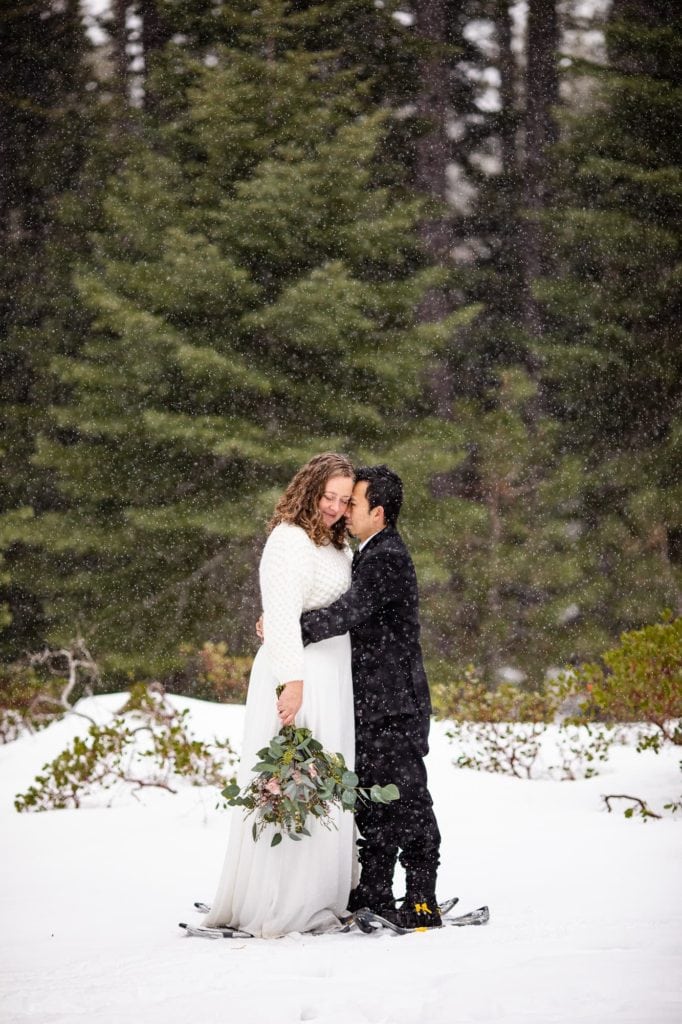 Close up of a bride and groom embracing in a snow filled forest